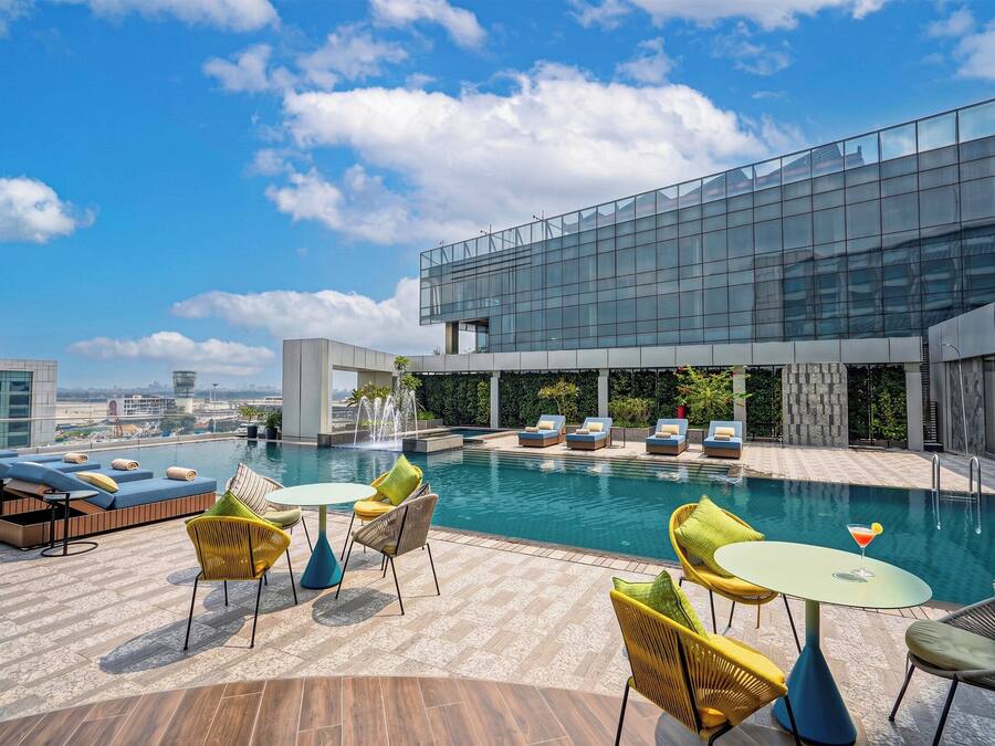 Un área de piscina en la azotea con sillones de descanso, una mesita y vistas del horizonte de la ciudad.