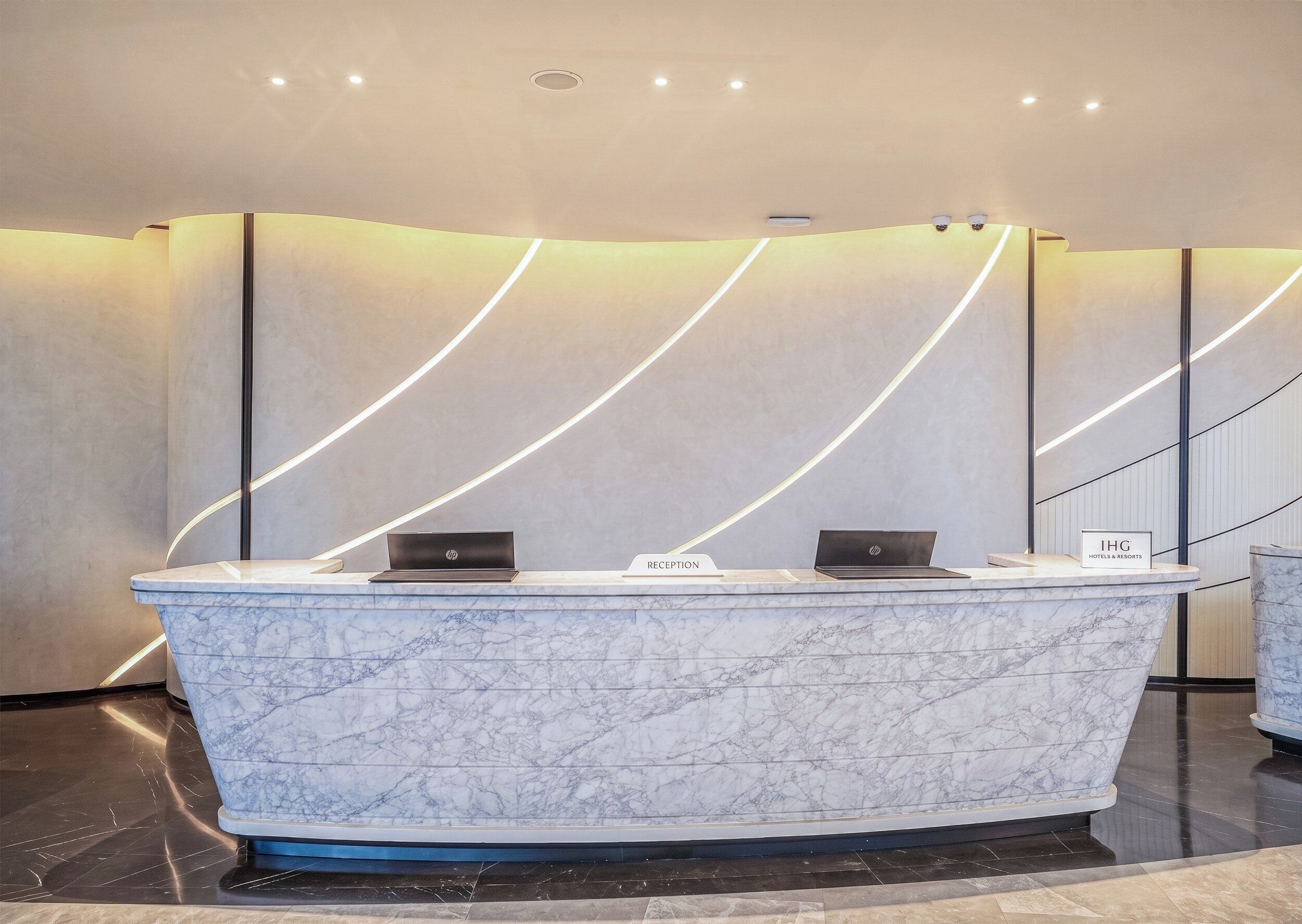 A reception desk with a marble top, two laptops, and a sign indicating 'IHG Hotels & Resorts.'