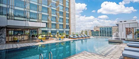 A modern hotel with a rooftop infinity pool, lounge chairs, and a bar area.