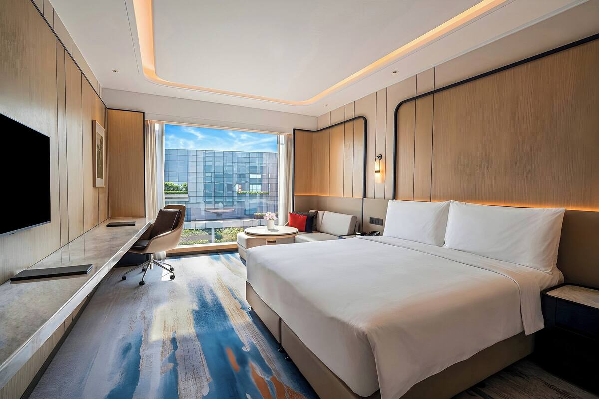 Ein modernes Hotelzimmer mit einem großen Bett, einem Schreibtisch, einem Sessel und einem Fernseher.