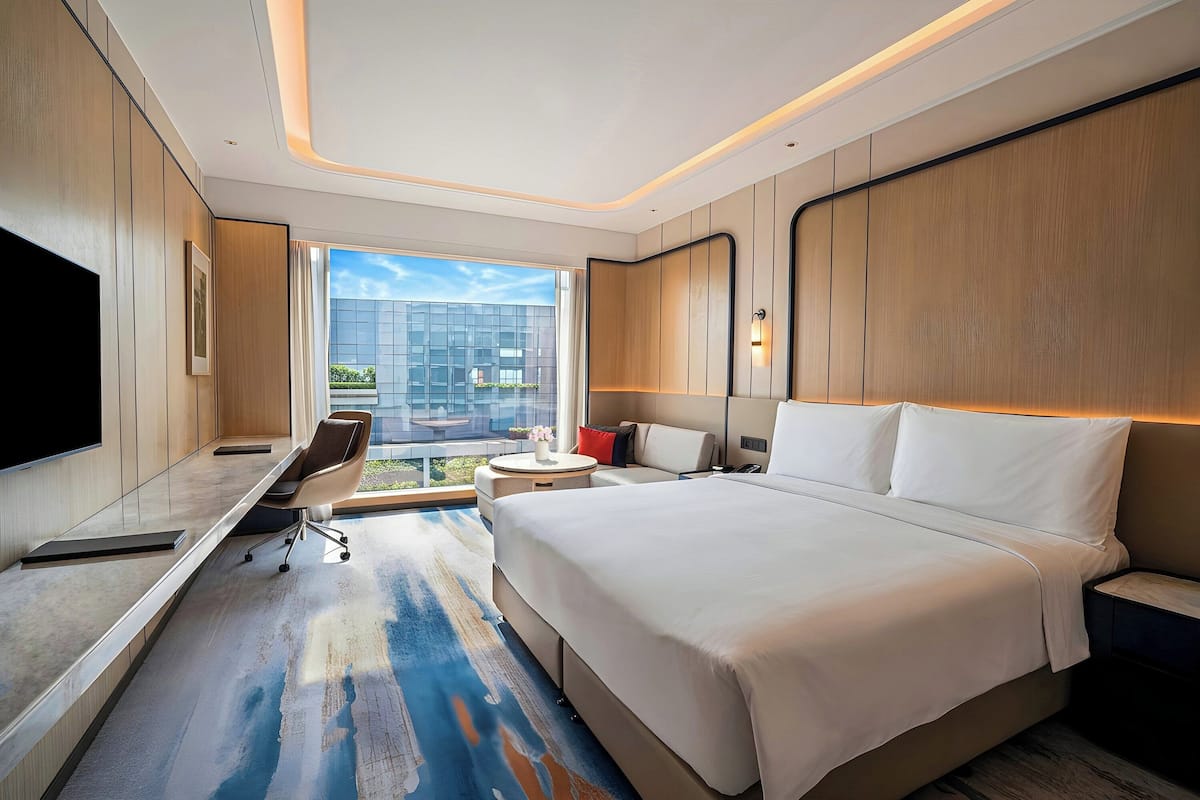 Ein modernes Hotelzimmer mit einem großen Bett, einem Schreibtisch, einem Sessel und einem Fernseher.