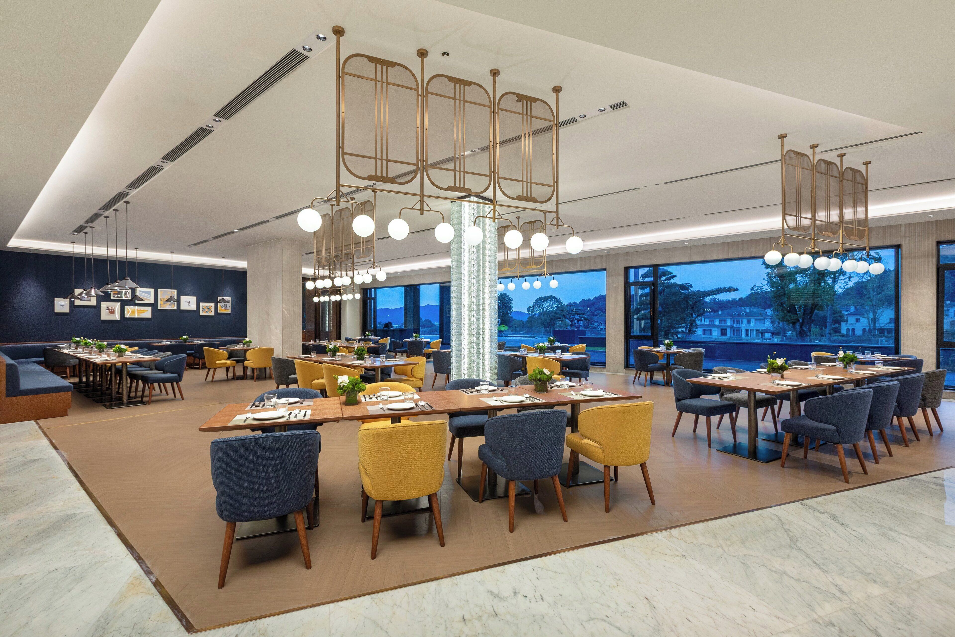 Un comedor moderno con varias mesas y sillas, ventanas amplias y un elegante lámpara decorativa.