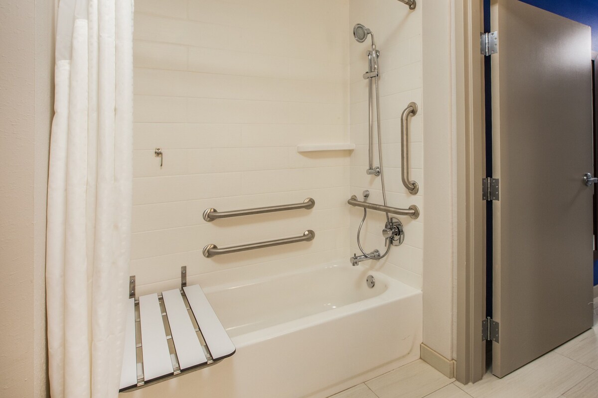 Une salle de bain moderne équipée d’une baignoire, de barres d’appui et d’un pommeau de douche.