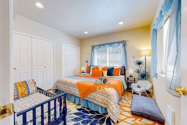 A bedroom decorated with orange and blue accents, double closets, and a toddler bed.
