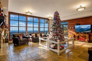 A spacious living room with a large window, a Christmas tree, leather sofas, and a television.