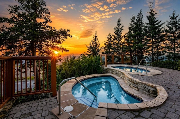 A swimming pool with a stone edge, surrounded by trees and a wooden fence.