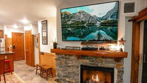 Een gezellig interieur met een stenen openhaard, een bevestigde televisie waarop een berglandschap te zien is, en een bar.