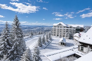 Un complejo turístico en la montaña cubierto de nieve, con un edificio grande, presumiblemente un hotel, que cuenta con varios pisos y una prominente bandera estadounidense.