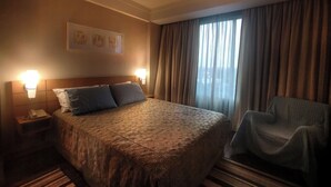 Habitación de hotel con una cama grande, una silla, una mesita de noche y una ventana con cortinas.