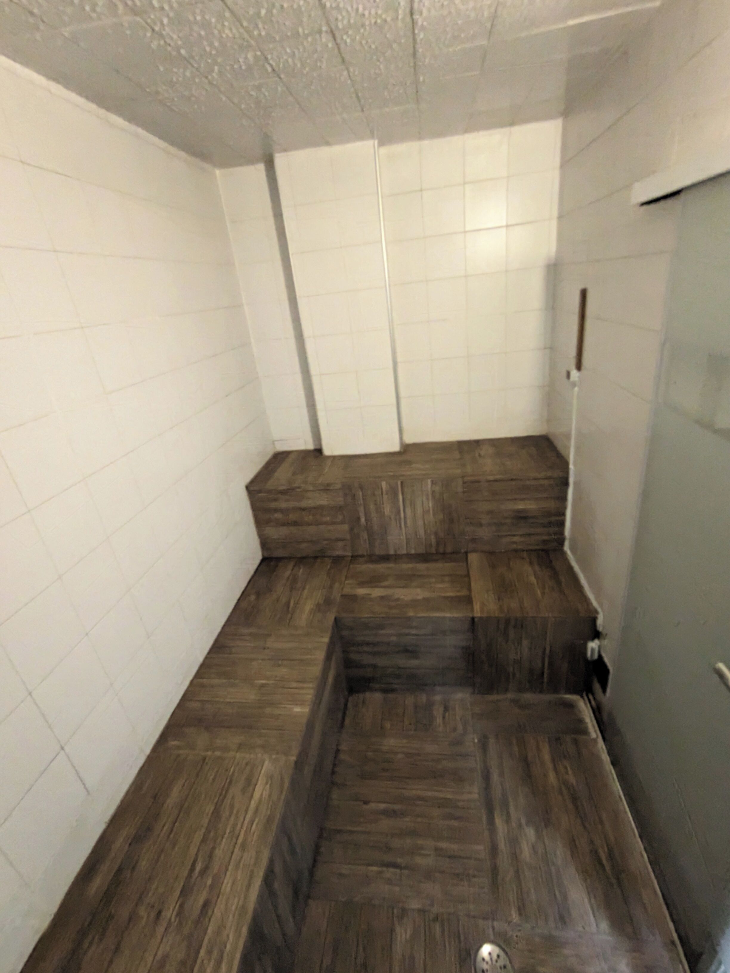 Une salle de bain avec des murs carrelés de carreaux blancs, un plancher en bois et un espace douche.