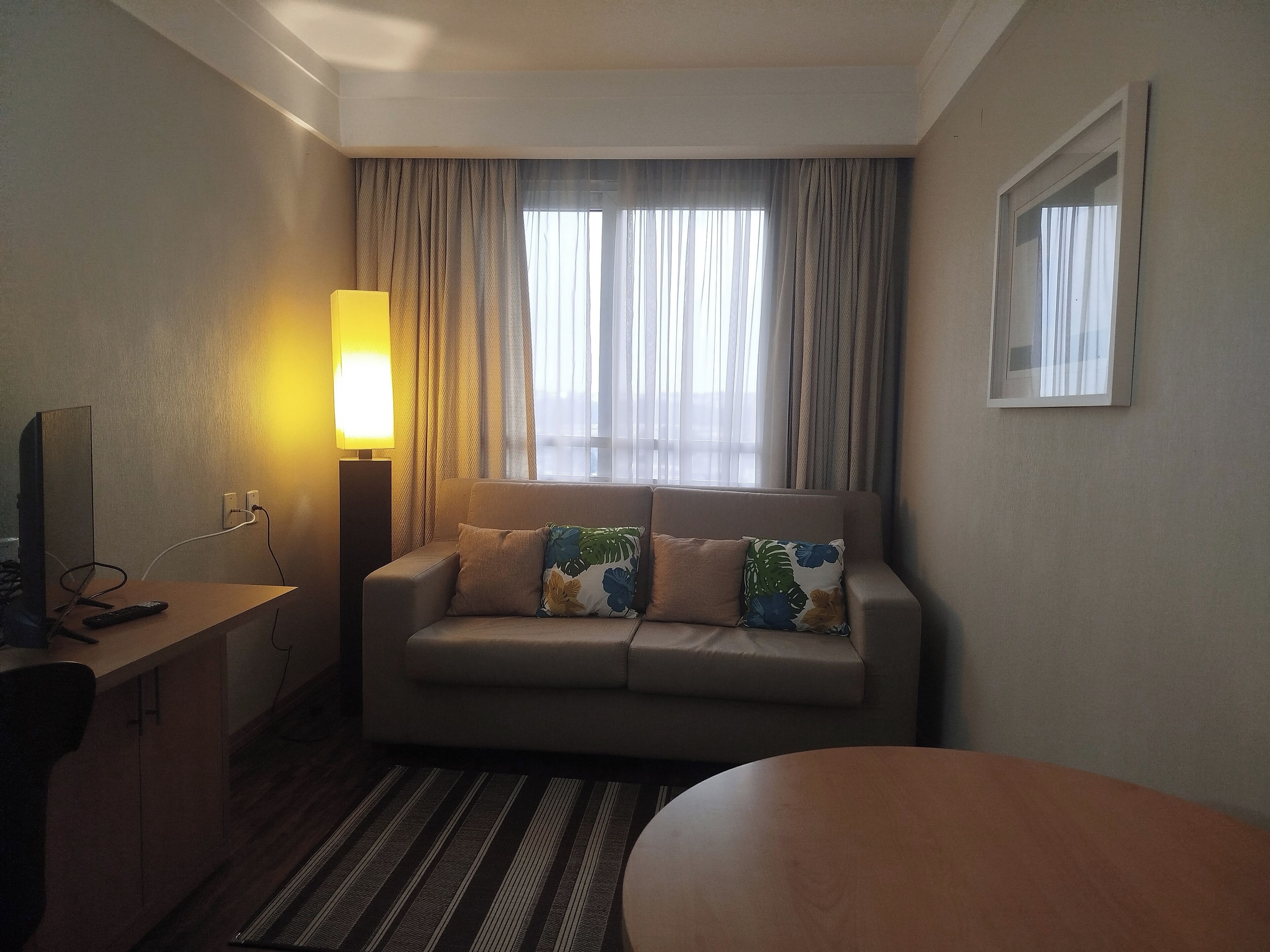 Habitación de hotel con sofá, una mesita, lámpara y ventana con cortinas.