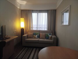 Habitación de hotel con sofá, una mesita, lámpara y ventana con cortinas.