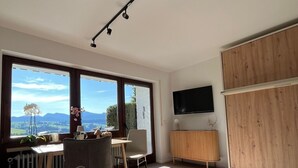 Moderni olohuone, jossa on suuri ikkuna, litteänäyttöinen televisio ja puinen kaappi.