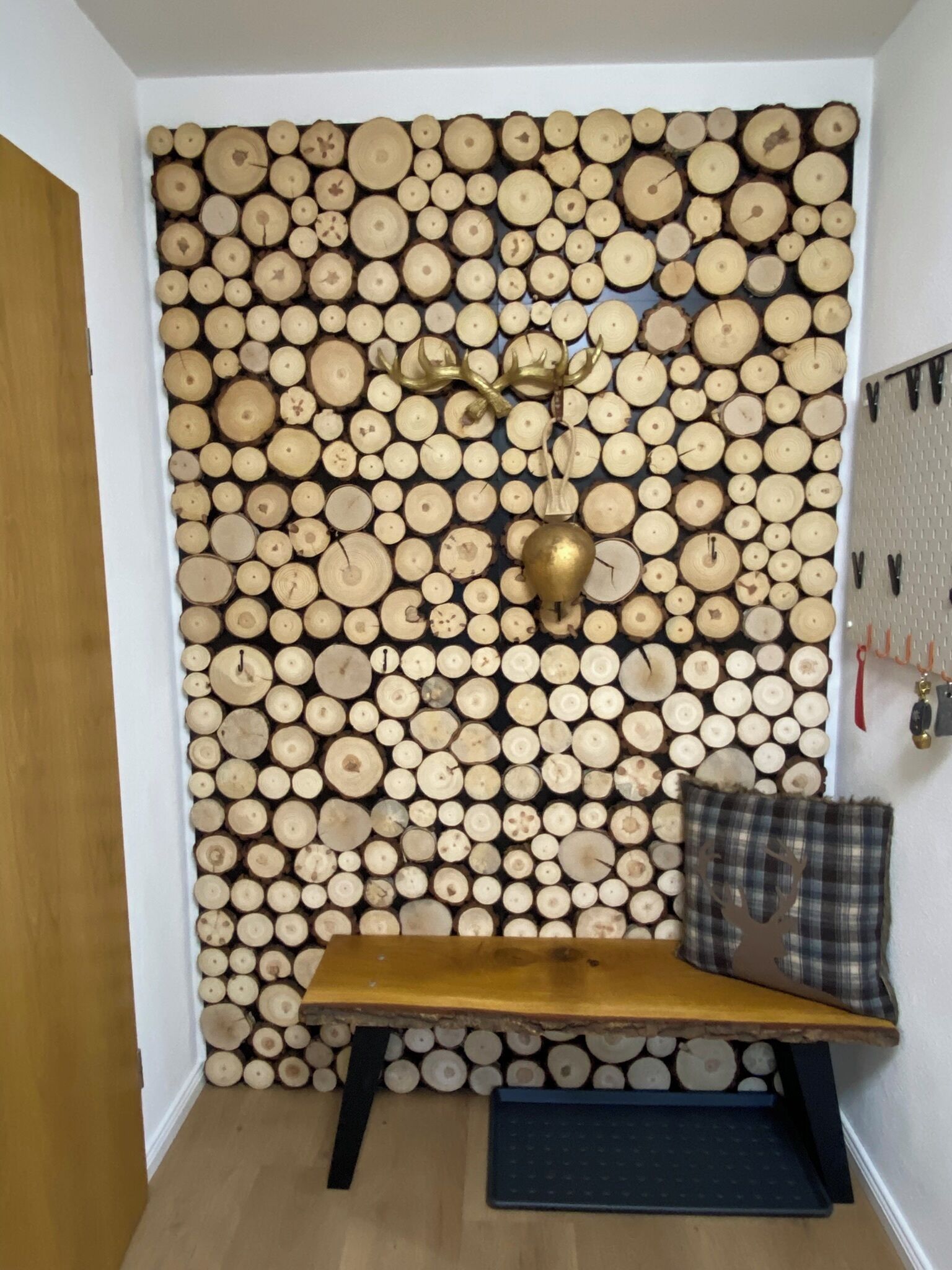 A room with a wall covered in stacked logs, a wooden bench, and a hanging coat rack.