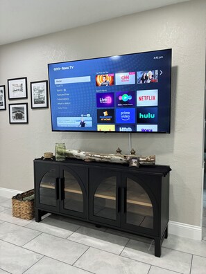 A flat-screen TV mounted on a wall displaying a Roku interface with various streaming services.