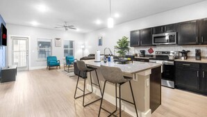 A modern kitchen with a central island, bar stools, dark cabinetry, and a ceiling fan. - Grand Prairie 2BR | IKEA, Epic Waters, Bass Pro (Grand Prairie)
