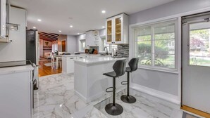 A modern kitchen with white cabinets, a marble countertop, and two black bar stools. - Marvelous 3-bedroom townhome with  Heated floor Manchester (Manchester)