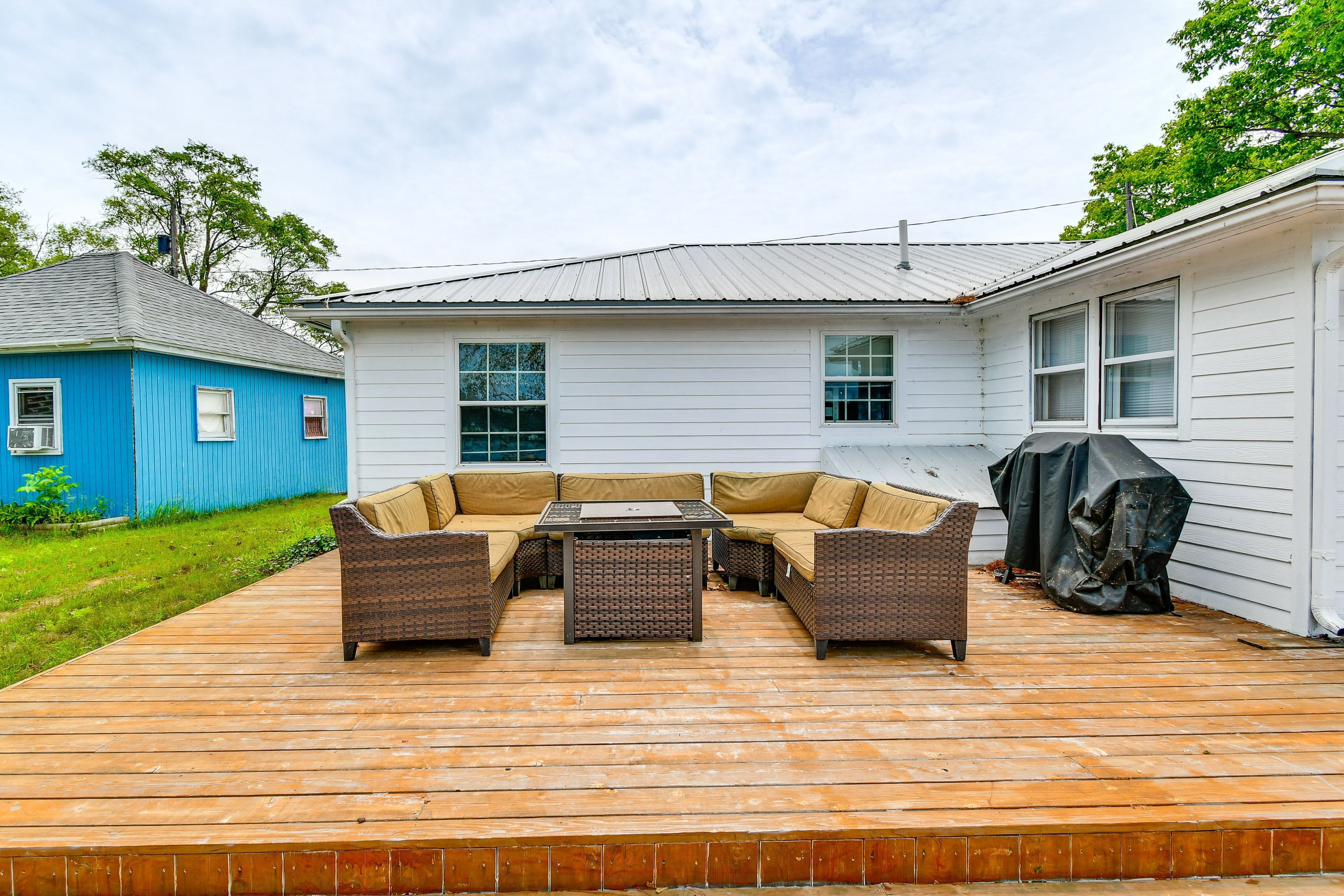 A wooden deck with a wicker sectional sofa and table set against the home's white exterior.