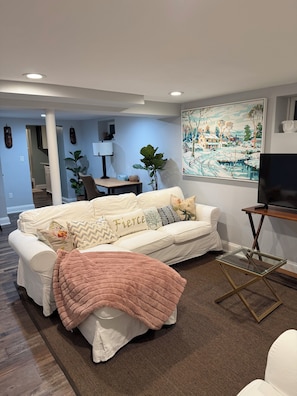 A living room with a sofa, a glass coffee table, a TV stand, and a painting on the wall. - Tremendous apartment in Fairfield for a cozy getaway (Fairfield)