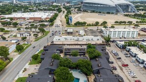 Un ampio parcheggio con diversi edifici, uno stadio e una strada con veicoli.