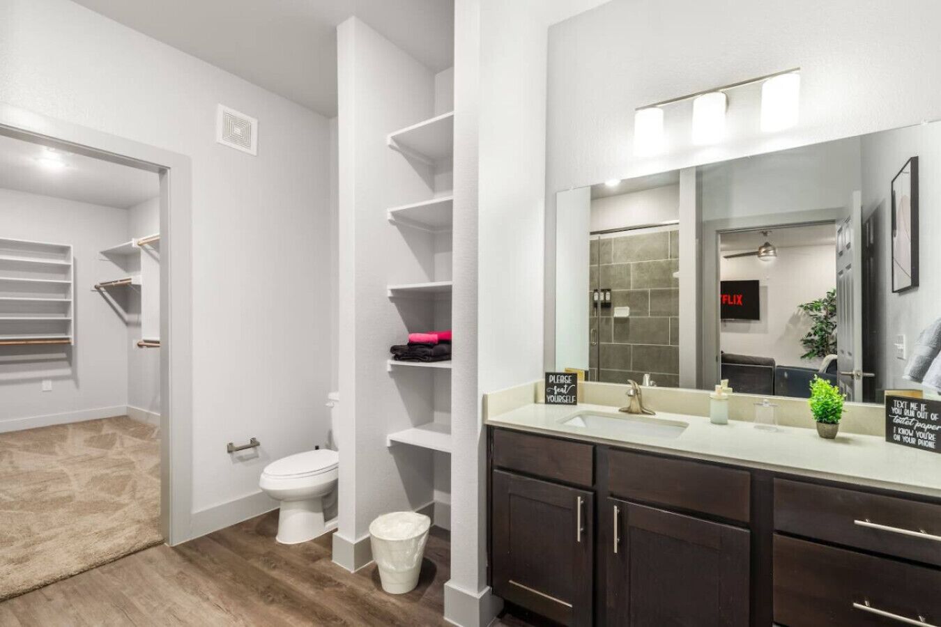 Ein modernes Badezimmer mit Toilette, Waschbecken und Waschtisch sowie ein begehbarer Kleiderschrank mit Regalen.