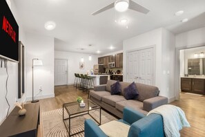 A modern living room with a sofa, coffee table, and a TV mounted on the wall. - Grand Prairie 1BR | IKEA, Epic Waters, Bass Pro (Grand Prairie)