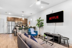 A modern apartment with a kitchen, living room, and a large flat-screen TV mounted on the wall. - Grand Prairie 1BR | IKEA, Epic Waters, Bass Pro (Grand Prairie)