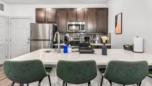 Una cucina moderna con elettrodomestici in acciaio inossidabile, mobili in legno scuro, un'isola bianca con sgabelli da bar e un quadro appeso al muro.