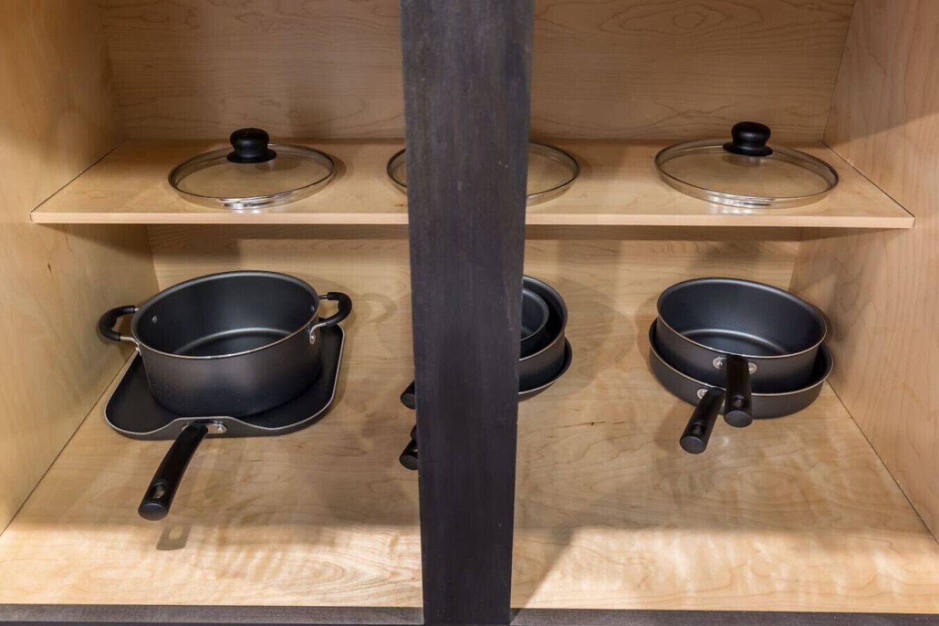 Une cuisine avec des étagères en bois, deux casseroles noires avec des couvercles et une autre casserole noire avec une poignée.