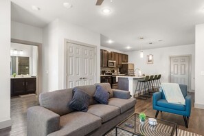 A modern living room with a sofa, a coffee table, and a blue chair. - Grand Prairie 1BR | IKEA, Epic Waters, Bass Pro (Grand Prairie)