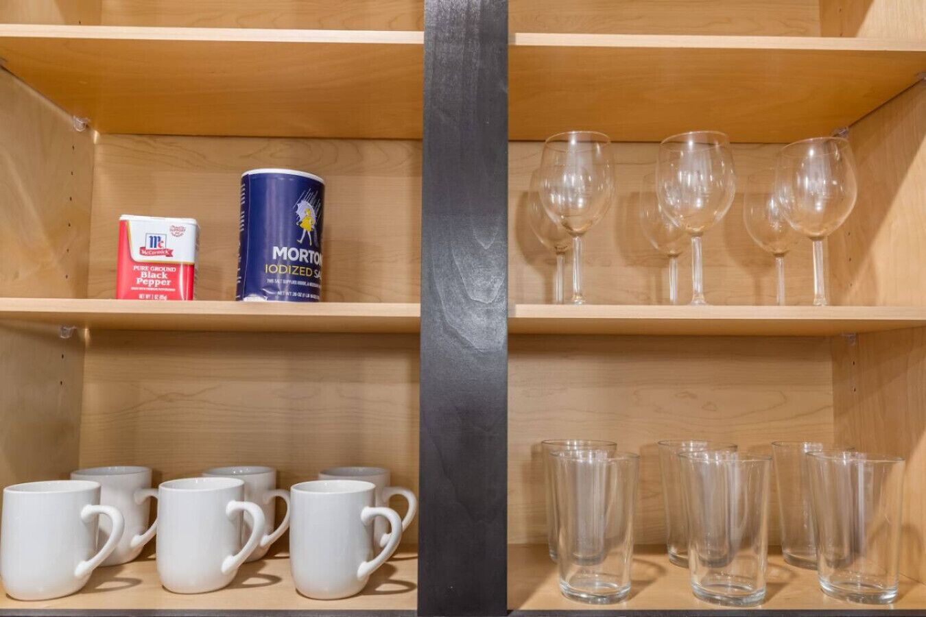 A shelf with white mugs, a Morton's Iodized Salt can, and wine glasses.