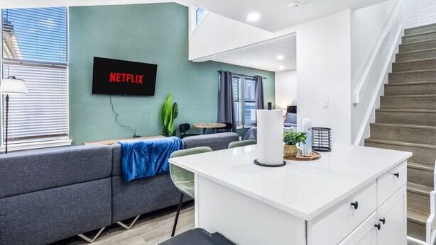 Ett modernt hotellrum med en soffa, ett litet bord, ett skrivbord, en trappa och en väggmonterad TV med texten ”NETFLIX”.