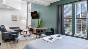 Ett modernt hotellrum med en säng, en soffa, ett skrivbord, en TV och stora fönster.