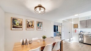 Una cocina moderna con armarios blancos, una mesa de comedor de madera y tres cuadros en la pared.