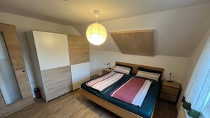 A bedroom with a wooden bed, a wardrobe, a bedside table, and a hanging light fixture. - Cozy apartment near the Bavarian Forest – ideal for couples or families (Neukirchen, Alemania)