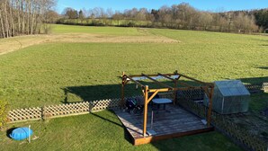 A wooden deck with a table and chairs, a covered area, and a shed in a grassy field. - Cozy apartment near the Bavarian Forest – ideal for couples or families (Neukirchen, Alemania)