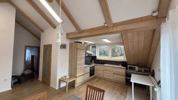 A modern kitchen with wooden beams, a dining area, and a view of the outdoors.
