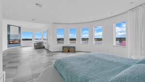 A modern bedroom with a large bed, a fireplace, a view of the outdoors, and a curved ceiling. - Elegant Waterfront Stay + Bay + Sunset Views (Sea Bright)