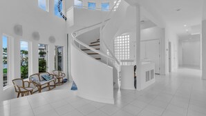 A spacious interior with a white spiral staircase, large windows, and a seating area with wicker furniture. - Elegant Waterfront Stay + Bay + Sunset Views (Sea Bright)