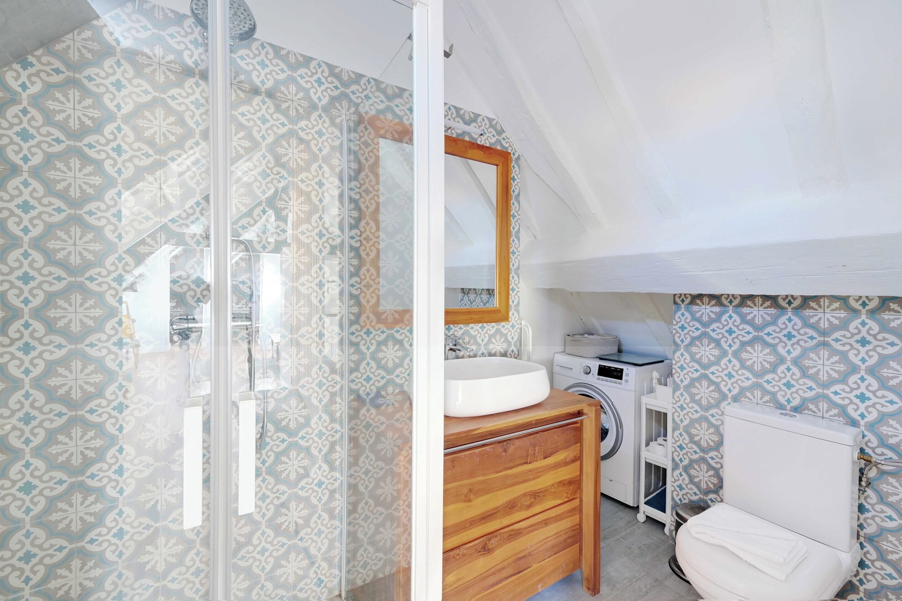 Une salle de bain avec des murs à motifs, un meuble-lavabo en bois, un évier, un miroir, des toilettes et un lave-linge.