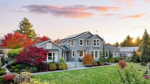 A two-story house with a front porch, a garage, and a well-maintained garden with various shrubs and trees. - 3-home Coastal Retreat w/ Sauna, Firepit & Greenhouse Seabright Haven by Avantstay (Coupeville)