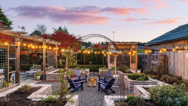 Une terrasse de jardin avec des sièges d’extérieur, un foyer et des guirlandes lumineuses.