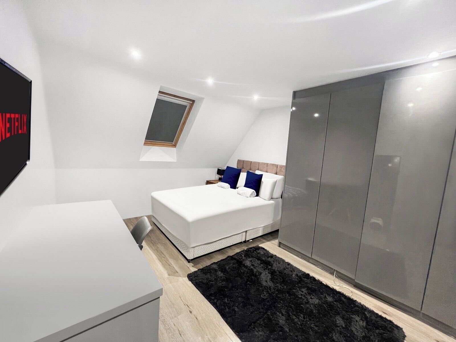 Un dormitorio moderno con cama, armario, escritorio y ventana.