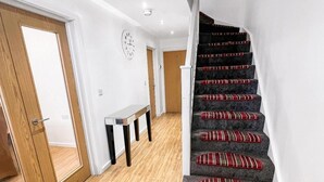 Eine Treppe mit rot-weiß gestreifter Teppichbelag, eine Holztür, eine weiße Wand mit einer Uhr und ein kleiner Tisch mit einem Spiegel.
