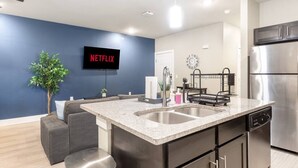 Eine moderne Küche mit einer großen Kochinsel, Edelstahlgeräten und einem Flachbildfernseher, der 'NETFLIX' anzeigt.