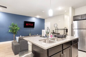 Una cocina moderna con una isla grande, electrodomésticos de acero inoxidable y un televisor de pantalla plana mostrando 'NETFLIX'.