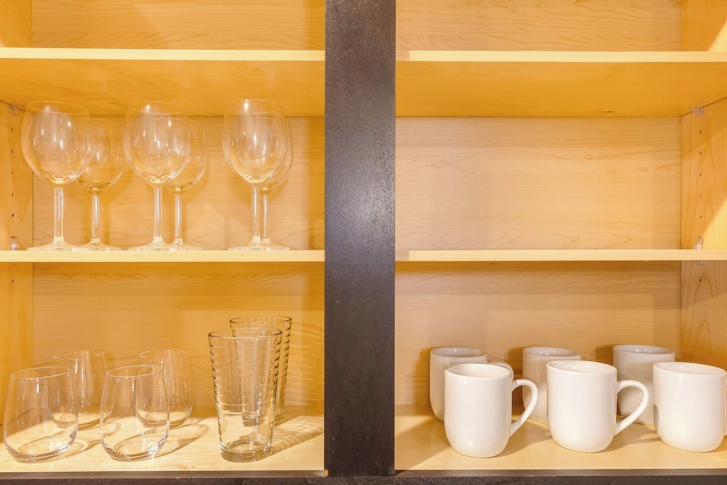 Een houten plankenwand met wijnglazen en witte mokken.