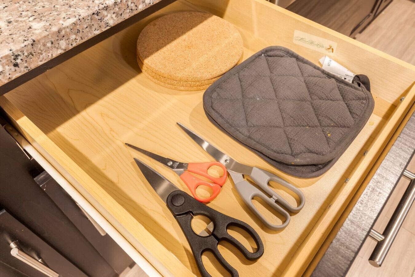 A drawer with a cork mat, a quilted pouch, and a pair of scissors.