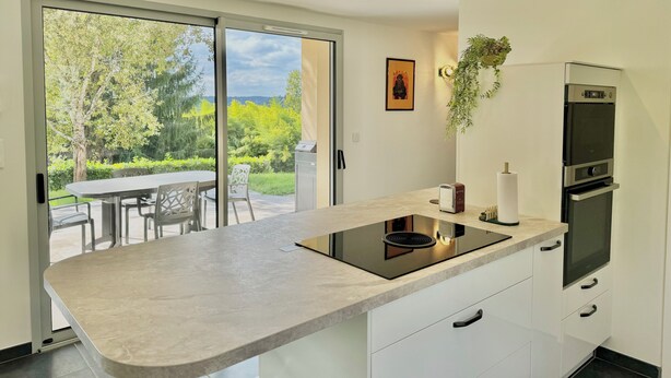 Una cocina moderna con una isla grande, horno empotrado y vistas a un jardín a través de puertas de cristal.