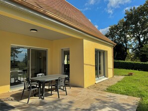 A yellow building with a patio area featuring a table and chairs, large sliding glass doors, and a well-maintained lawn. - Bungalow, air conditioning, 700 m from downtown (Sarlat-la-Canéda)